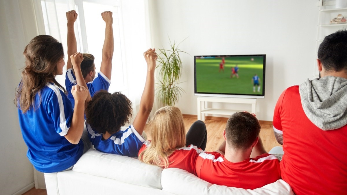 Rodina a přátelé sledují fotbal v obýváku a slaví gól