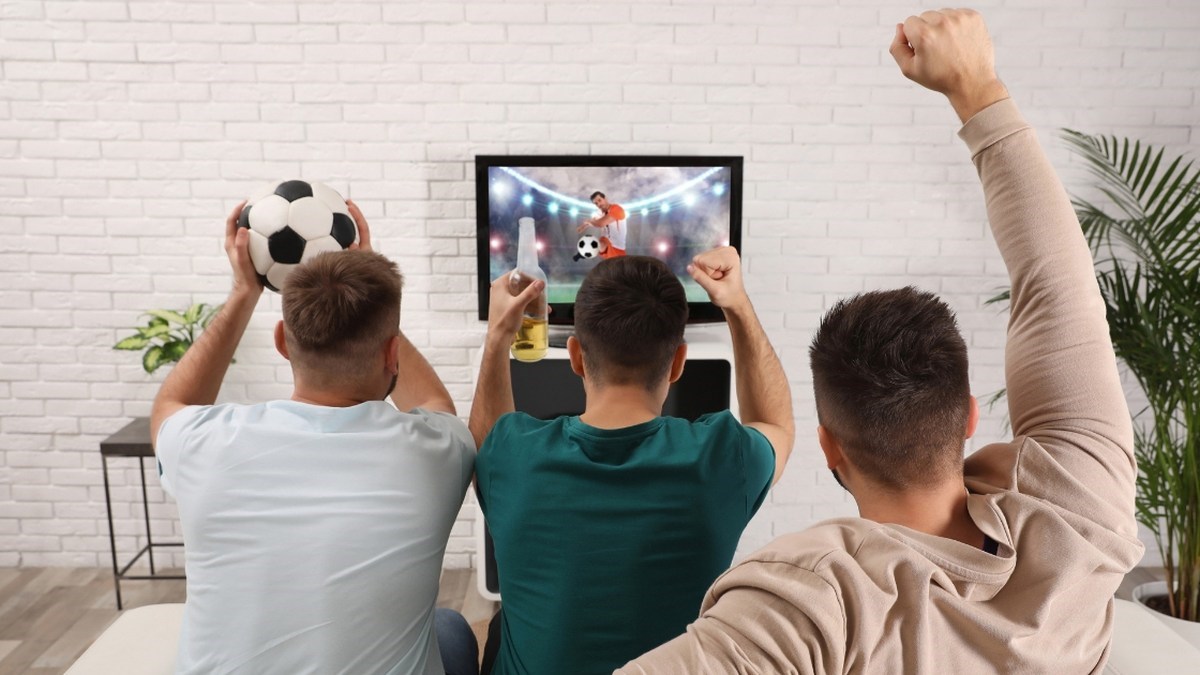 Tři fanoušci sledují fotbalový zápas na televizi a oslavují akci